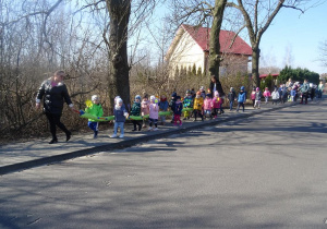 Dzieci wraz z paniami maszerują ulicami osiedla, śpiewają wiosenne piosenki.
